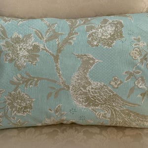 Könnte beinhalten: Rechteckiges Zierkissen mit einem Vogel- und Blumenmuster in Beige und Weiß auf hellblauem Hintergrund. Das Kissen liegt auf einem gemusterten Stuhl.