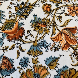 May include: Close-up of a white fabric with a repeating floral pattern. The design features stylized flowers in shades of orange, teal, and brown, with black outlines. The floral elements are arranged in a flowing, organic style.