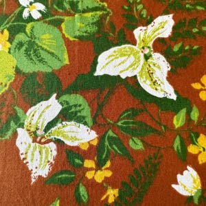 Könnte beinhalten: Nahaufnahme eines Blumenmusters mit weißen Blüten mit gelben und grünen Akzenten, grünen Blättern und kleinen gelben Blüten auf einem rotbraunen Hintergrund. Das Design hat eine Vintage-Ästhetik.