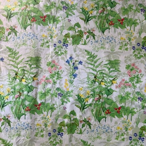 Könnte beinhalten: Ein weißer Stoff mit einem sich wiederholenden Blumenmuster. Das Design zeigt verschiedene Blumen in Rot-, Rosa-, Gelb-, Blau- und Lilatönen sowie grünes Laub. Der Gesamteffekt ist ein lebendiger, botanischer Druck.