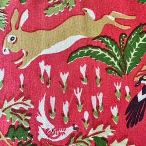 Puede incluir: Una tela roja con un patrón repetido de un conejo corriendo en beige y blanco, follaje verde y elementos florales estilizados blancos y verdes. El diseño tiene un aspecto vintage y caprichoso.