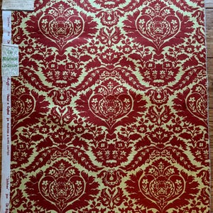 Könnte beinhalten: Ein Stoffstück mit einem sich wiederholenden Damastmuster in Rot und Hellgelb. Das Design umfasst florale und herzförmige Motive. Der Stoff hat ein Etikett mit der Aufschrift "The Belgravia Collection".