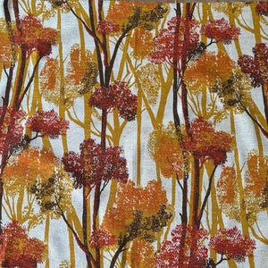 Op de afbeelding: Stof met een herhaald patroon van gestileerde bomen in herfstkleuren. Het ontwerp toont bruine, oranje en gele bomen tegen een witte achtergrond. De stof is waarschijnlijk bedoeld voor woondecoratie of kleding.