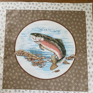 以下が含まれることがあります： 円形のフレーム内に、跳ねる虹鱒のイラストが描かれた正方形の布パネル。 虹鱒は、青と白の水色の背景に、ピンク、緑、茶色の鱗で描かれています。 パネルには、茶色と白の模様のボーダーがあります。