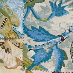 Puede incluir: Primer plano de muestras de tela con un estampado floral. El diseño presenta grandes flores y hojas estilizadas en tonos de azul, verde y amarillo sobre un fondo crema. Los bordes de la tela están sobrehilados.