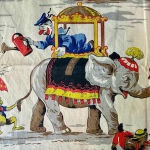 May include: Vintage circus-themed fabric featuring an elephant with a clown riding on its back. The fabric has a repeating pattern with other circus characters, including a monkey with an umbrella, a clown, and a duck in a cart. The color palette includes red, blue, yellow, and gray.