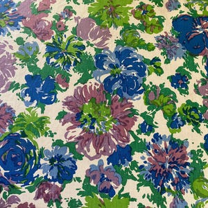Könnte beinhalten: Stoff mit einem sich wiederholenden Blumenmuster. Das Muster zeigt große Blüten in Blau, Lila und Grün auf cremefarbenem Hintergrund. Die Blumen haben einen handgemalten Look, der dem Textil einen farbenfrohen, Vintage-Look verleiht.