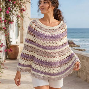 Può includere: Un poncho all'uncinetto con strisce orizzontali color crema, viola chiaro e tortora. Il capo presenta un motivo traforato, un'ampia scollatura rotonda e un bordo smerlato lungo l'orlo inferiore, indossato sopra un top di colore chiaro.