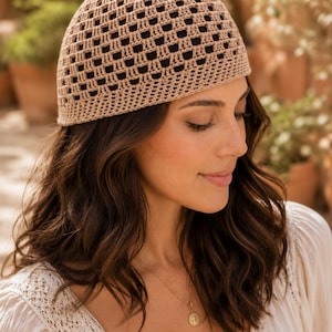 Puede incluir: Un gorro de ganchillo beige con un patrón de rejilla cuadrada repetitivo. El gorro está construido con un tejido denso y estructurado que crea una serie de ventanas cuadradas abiertas y oscuras en la corona y los lados, con una banda.
