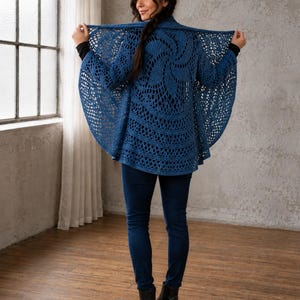 May include: A deep blue crochet cardigan featuring an intricate circular mandala-style pattern on the back, long sleeves, and an open-front design. The garment is paired with dark blue denim jeans and black leather ankle boots for a complete look.