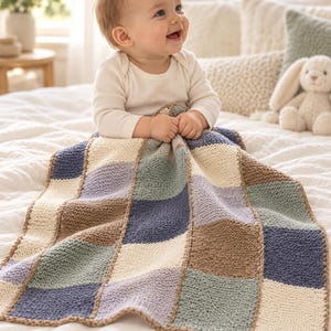 Könnte beinhalten: Eine Babydecke mit einem Patchwork-Design aus gestrickten Quadraten in den Farben Marineblau, Creme, Salbeigrün, Hellviolett und Hellbraun. Die Decke hat ein strukturiertes kraus rechts gestricktes Muster und sichtbare Nähte zwischen den Quadraten.