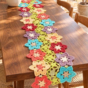 Puede incluir: Un camino de mesa rectangular de ganchillo con un patrón repetitivo de flores de seis pétalos en tonos rojo, coral, amarillo claro, turquesa y morado, unidas por una red calada de color verde claro con motivos florales pequeños.