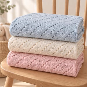 May include: A stack of three folded knitted blankets in light blue, cream, and soft pink. Each blanket features a consistent diagonal eyelet pattern with delicate openwork detailing throughout the fabric, creating a textured and uniform appearance.
