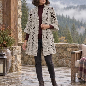 Könnte beinhalten: Eine beige, vorne offene Häkelstrickjacke mit strukturiertem, geometrischem Muster, Dreiviertelärmeln und breitem Kragen, getragen über einem dunkelweinroten Rollkragenpullover, einer dunklen Hose und dunkelbraunen Lederstiefeletten.