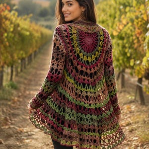 Könnte beinhalten: Eine langärmelige Häkeljacke mit einem kreisförmigen, von Mandalas inspirierten Muster auf der Rückseite. Das Kleidungsstück ist aus mehrfarbigem Garn in den Tönen tiefes Magenta, Olivgrün und Erdbraun gefertigt und zeigt ein durchbrochenes Spitzenmuster.