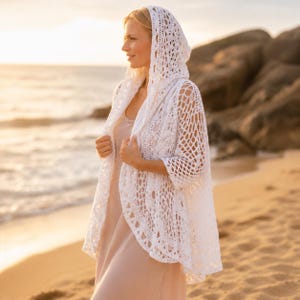 May include: A white hooded cardigan featuring an intricate openwork crochet pattern with a net-like design. The garment has three-quarter length sleeves, a draped open front, and a pointed hood, crafted from lightweight white yarn in a delicate style.