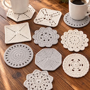 Puede incluir: Una colección de nueve posavasos de ganchillo en varias formas, incluyendo círculos, cuadrados, hexágonos y octágonos, en colores hilo blanco roto y gris claro. Dos tazas de cerámica blanca con café negro descansan sobre dos posavasos.