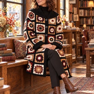 Può includere: Un cardigan lungo a maniche lunghe realizzato con un patchwork di quadrati all'uncinetto nei toni del nero, crema, marrone chiaro e rosso scuro. Il capo presenta un colletto nero a tinta unita, polsini neri e chiusura frontale a tre bottoni.