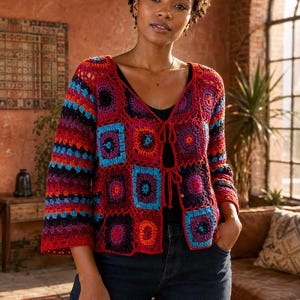 May include: A long-sleeved crochet cardigan featuring a vibrant granny square pattern in shades of red, blue, purple, and orange. The garment has a V-neckline, three-quarter length sleeves, and two thin tie closures at the center front of the bodice.