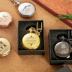 Puede incluir: Variedad de relojes de bolsillo personalizados en oro, plata y oro rosa. Algunos relojes están grabados con iniciales, nombres y un paisaje de montaña. Varios relojes se muestran en cajas de regalo negras, con cadenas y cierres.