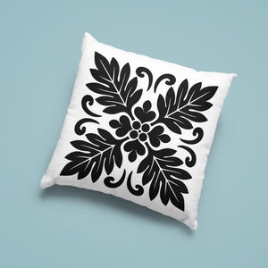 May include: White square pillow with a black floral design. The pattern features stylized leaves and swirling accents, creating a symmetrical, decorative motif. The pillow is set against a light blue background.