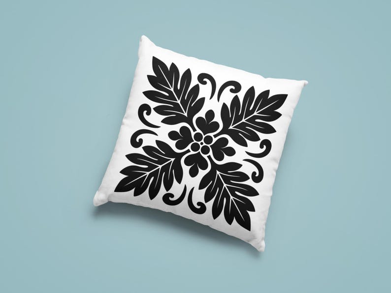 May include: White square pillow with a black floral design. The pattern features stylized leaves and swirling accents, creating a symmetrical, decorative motif. The pillow is set against a light blue background.