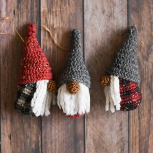 Peut inclure: Trois ornements de gnome en crochet avec des barbes en laine blanche. Les gnomes ont des chapeaux de différentes couleurs : rouge, gris et noir et rouge à carreaux.