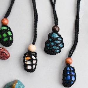 Puede incluir: Cuatro collares de ganchillo con piedras de diferentes colores en su interior. Cada collar tiene una cuenta de madera en la parte superior. Las piedras son verdes, azules, blancas y azules.