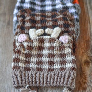 May include: Three crocheted hats stacked on top of each other. The top hat is orange with white polka dots, the middle hat is black and white checked, and the bottom hat is brown and white with a braided tassel.