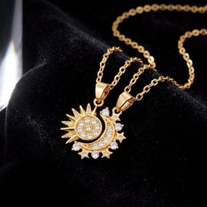 May include: Gold-toned necklace featuring two pendants: a sun and a crescent moon. The sun pendant has a circular center with small, clear stones and radiating rays. The moon pendant is adorned with similar stones and star accents. The necklace chain is delicate.