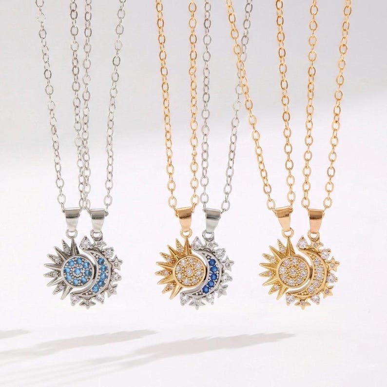 May include: Three necklaces with sun and moon pendants. The pendants are split, with one half a sunburst design and the other a crescent moon. The sunbursts are gold or silver, and the moons are blue or clear. The chains are gold or silver.