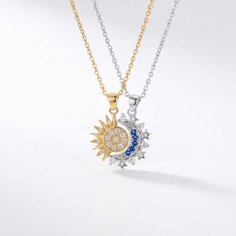 May include: Two necklaces with celestial pendants. One pendant is a gold sunburst with a circle of clear stones. The other is a silver crescent moon with blue and clear stones. Both necklaces have delicate chains.