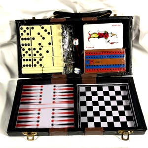 May include: A black, brown, and tan travel game set. The set includes dominoes, dice, playing cards, a backgammon board, and a checkerboard. The set is in an open, black case with a handle and gold-colored clasps.