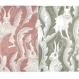 May include: Two panels of fabric featuring a repeating pattern of white rabbits and foliage. One panel has a dusty rose background, and the other has a muted green background. The design is reminiscent of a vintage botanical illustration.