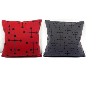 May include: Two square throw pillows. One is red with a black geometric pattern of connected circles. The other is gray with a similar black pattern. Both pillows have a solid color on the back.