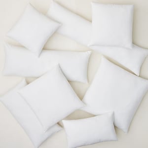 May include: An assortment of white pillows in various shapes and sizes, including square, rectangular, and long bolster pillows. The pillows are arranged on a light-colored surface, showcasing their clean, simple design. Ideal for home decor and bedding.