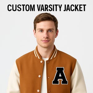 May include: A brown and cream varsity jacket with the text "CUSTOM VARSITY JACKET" at the top. The jacket has a large black "A" on the chest. The jacket has cream-coloured sleeves and striped cuffs and collar.