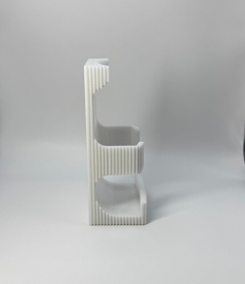 Puede incluir: Un organizador vertical blanco impreso en 3D con un dise&ntilde;o acanalado. Cuenta con dos estantes curvos y una secci&oacute;n superior, adecuado para guardar objetos peque&ntilde;os. El organizador est&aacute; hecho de pl&aacute;stico de color claro.