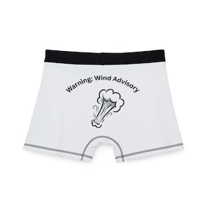 May include: White boxer briefs with a black waistband and gray stitching. The briefs feature the text "Warning: Wind Advisory" above a cartoon illustration of a cloud with wind lines.