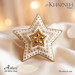 May include: A three-dimensional star ornament crafted from white and metallic gold beads. The center features a cluster of faceted gold beads, surrounded by a geometric pattern of white and gold seed beads. Text reads Al Khazneh Designs, Asteri 3D Mini Star, and Planbead.com.