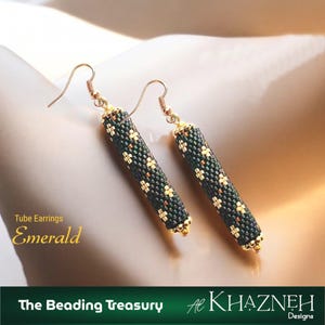 May include: Emerald tube earrings with a beaded design. The earrings are cylindrical, with a dark green and gold pattern. The earrings have gold-coloured hooks and accents. The text "Tube Earrings Emerald" is visible.
