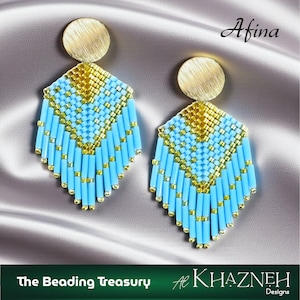 以下が含まれることがあります： ゴールドのディスクのトップとダイヤモンド型のペンダントが付いた、手作りのイヤリングのペア。ペンダントは、水色とゴールドのビーズのパターンで、青いビーズのフリンジが付いています。イヤリングはサテンの表面に表示されています。