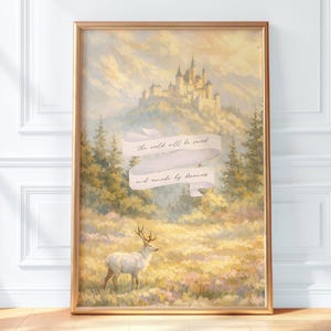 Puede incluir: Una lámina de arte enmarcada con un paisaje de un ciervo blanco en un prado dorado con un castillo en una colina lejana. Una cinta blanca en el centro muestra el texto, the world will be saved and made by dreamers.