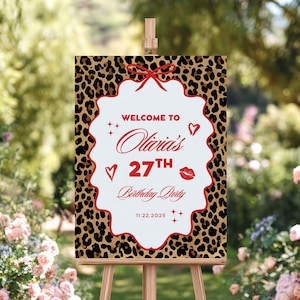 Puede incluir: Un letrero de fiesta de cumplea&ntilde;os sobre un caballete, con un borde de estampado de leopardo. El centro blanco del letrero tiene texto rojo: "Bienvenida a la fiesta de cumplea&ntilde;os n&uacute;mero 27 de Olivia" y la fecha 11.22.2025. Decorado con corazones, estrellas y un lazo rojo.