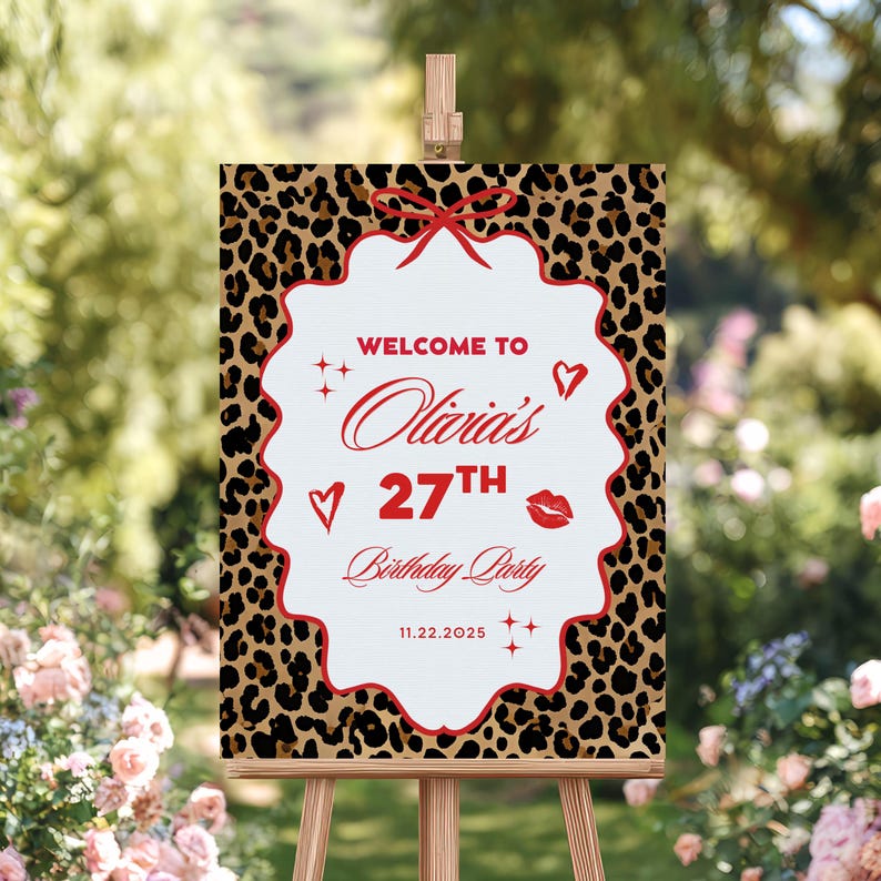 Puede incluir: Un letrero de fiesta de cumplea&ntilde;os sobre un caballete, con un borde de estampado de leopardo. El centro blanco del letrero tiene texto rojo: "Bienvenida a la fiesta de cumplea&ntilde;os n&uacute;mero 27 de Olivia" y la fecha 11.22.2025. Decorado con corazones, estrellas y un lazo rojo.
