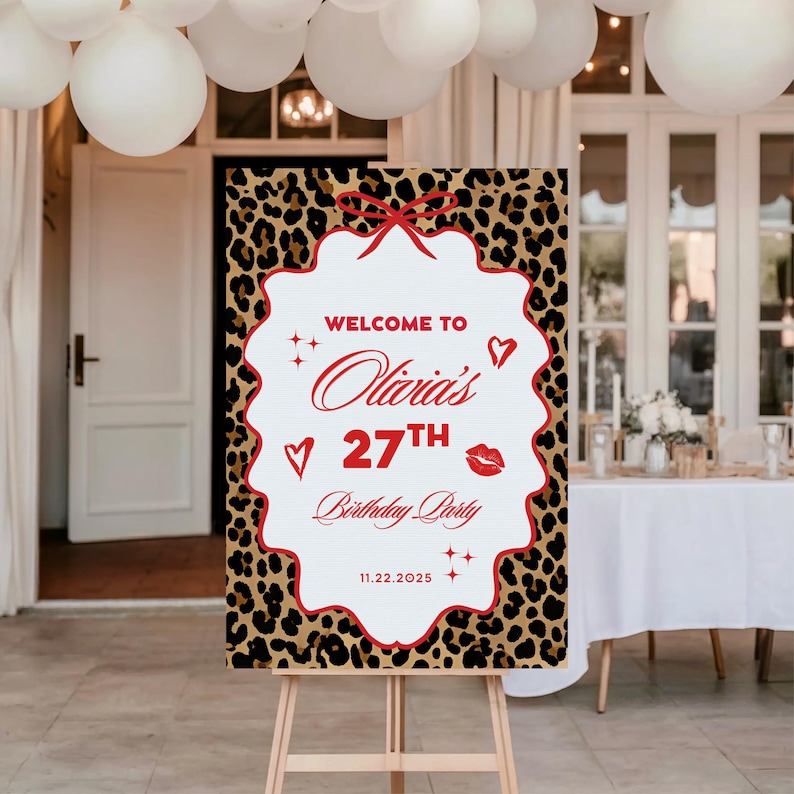 Puede incluir: Un letrero de bienvenida para una fiesta con un fondo de estampado de leopardo y un marco blanco festoneado. El letrero dice "Bienvenida a la fiesta de cumplea&ntilde;os n&uacute;mero 27 de Olivia" en escritura roja e incluye un lazo rojo, corazones y una marca de beso. Tambi&eacute;n se muestra la fecha 11.22.2025.