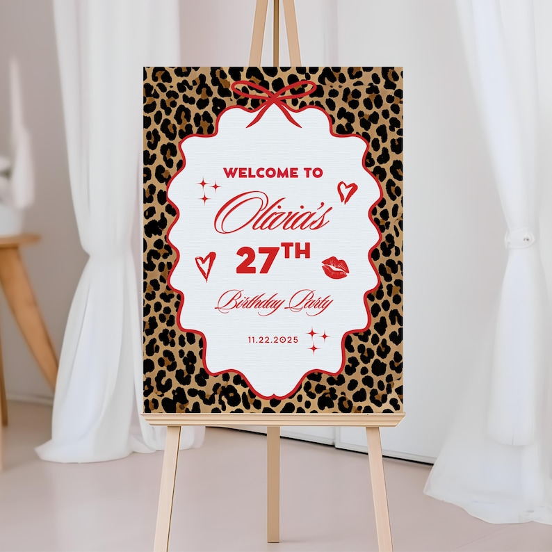 Puede incluir: Un letrero sobre un caballete con un fondo de estampado de leopardo. El letrero tiene un borde blanco festoneado con detalles en rojo y un lazo rojo en la parte superior. El texto dice "Bienvenida a la fiesta de cumplea&ntilde;os n&uacute;mero 27 de Olivia" con la fecha 11.22.2025.