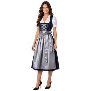 Op de afbeelding: Een marineblauwe dirndl-jurk met een witte blouse met korte pofmouwen en een kanten halslijn. Het lijfje heeft een zilverkleurige vetersluiting aan de voorzijde en de rok is gecombineerd met een glanzend zilveren schort gestrikt in de taille.