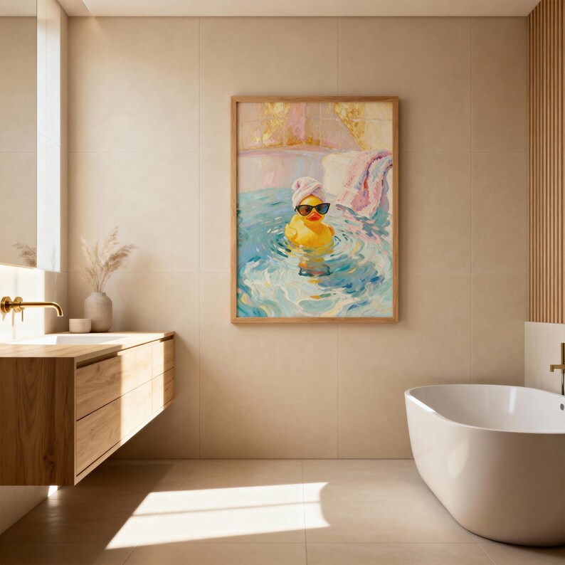 May include: A framed painting depicts a yellow rubber duck wearing sunglasses and a towel on its head, relaxing in a blue and white water scene. The artwork is in a wooden frame and hangs on a beige tiled wall in a bathroom setting.