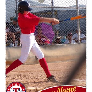 May include: Baseball action shot featuring a batter in a red jersey, white pants, and red socks. The batter swings a bat with blue and orange accents. The image includes a team logo and the words "Player Name" and "Outfield".